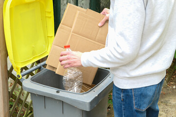 A man sorting waste. A person throwing cardboard packaging and a plastic bottle into a yellow...