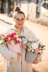 Young girl florist with two lush flower bouquets with fresh roses, eustomas, alstroemerias and eucalyptus branches in gift boxes outdoors