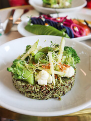 A plate of quinoa salad with pesto pistachio topped with boiled broccoli, green apple and sliced avocado, grounded nuts with creamy whipped Feta