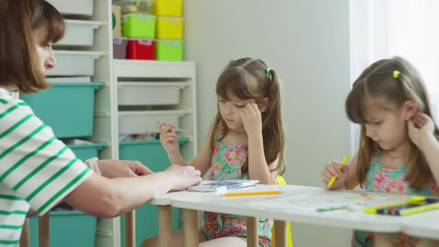The teacher helps two twin girls with their homework. Intellectual development of a child in a lesson in primary school. High quality 4k footage
