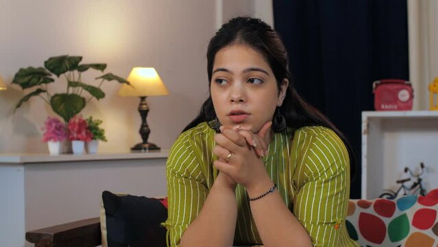 Beautiful Indian woman sitting alone with a headache at home  acute pain - health concept  modern day lifestyle. Upset Indian woman feeling weak  frustrated  lonely  and anxious  regretting the mis...
