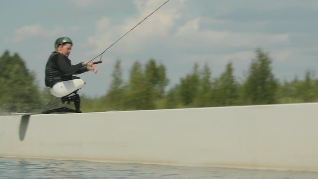 Caucasian teenage boy with no legs performing tricks on adaptive wake board in water outdoors on sunny day