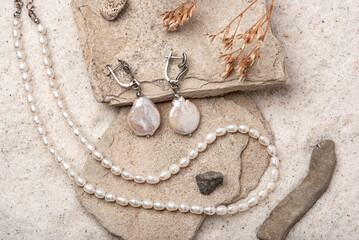 Beautiful Pearl Jewelry on white stones and sand. Necklace and earrings made of silver.