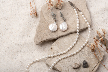 Beautiful Pearl Jewelry on white stones and sand. Necklace and earrings made of silver.