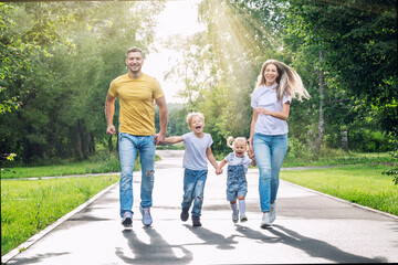 Happy family with two children joyfully run in the park on a sunny summer day. Parents, son and daughter in jeans and T-shirts. Love, tenderness and relationships in the family.