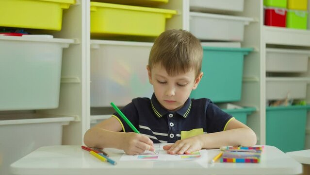 The boy chooses the pencil he needs and completes the task. Exercises in elementary school with elements of drawing. High quality 4k footage