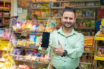 Young indian man showing smartphone screen at grocery shop.