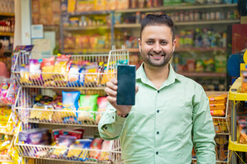 Young indian man showing smartphone screen at grocery shop.