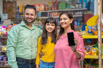 Happy indian family showing smartphone Screen at grocery shop.