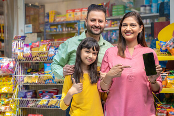 Happy indian family showing smartphone Screen at grocery shop.