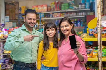 Happy indian family showing smartphone Screen at grocery shop.