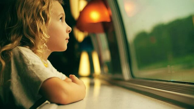 Happy little blonde girl looks through the window while traveling by train