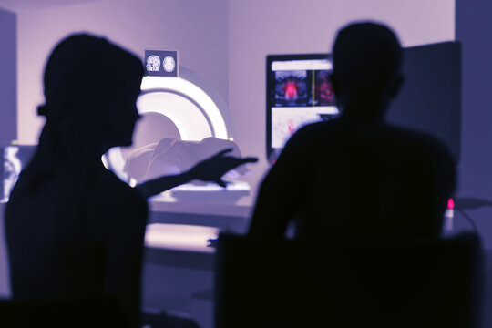 In Control Room Doctor and Radiologist Discuss Diagnosis while Watching Procedure and Monitors Showing Brain Scans Results, In the Background Patient Undergoes MRI or CT Scan Procedure.3D rendering .