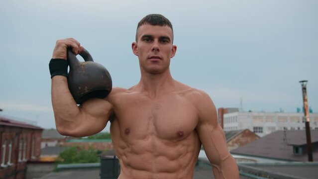 Bodybuilder holds kettlebell on his forearm and shows thumbs up after demonstrating biceps. Slow motion