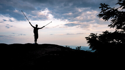 Silhouette of a happy and successful hiker at the summit, over the horizon at dusk