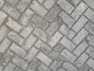 Stone pathway with unique tile pattern. Textured concrete paving for outdoor design. Urban cobblestone pavement, weathered tiles. Weathered gray bricks in herringbone pattern