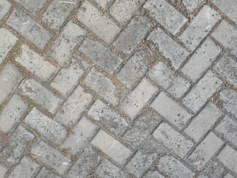 Stone pathway with unique tile pattern. Textured concrete paving for outdoor design. Urban cobblestone pavement, weathered tiles. Weathered gray bricks in herringbone pattern