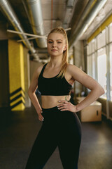 Confident young woman in fashion sporty outfit standing alone in a gym after a workout session