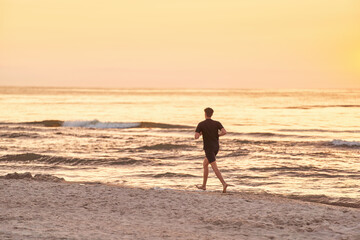Fototapeta na wymiar Endless Stride. Young Man's Sunset Run Along the Ocean Beach. Running on the sea beach.