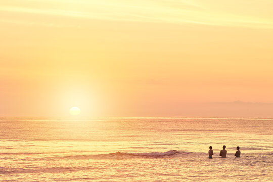 Silhouettes of a young group of people swimming in the ocean at sunset © AlexGo