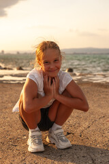 A girl dressed in a white dress is sitting on the pier. Smiling and looking ahead. The sea is restless and overcast before a thunderstorm
