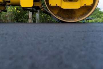 Yellow heavy vibrating roller on asphalt pavement Road construction, repairing rural road, sunny summer day. heavy equipment