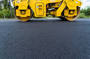 Yellow heavy vibrating roller on asphalt pavement Road construction, repairing rural road, sunny...