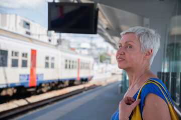 Active aged woman waiting for the train on the platform at the city station