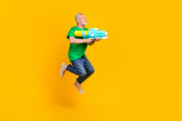 Fototapeta na wymiar Full body profile photo of overjoyed aged person jumping hold water gun empty space isolated on yellow color background