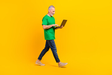 Full body profile portrait of nice aged man walking hold use wireless netbook isolated on yellow color background