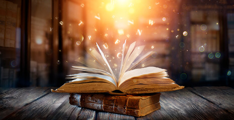 Old Book With Magic Lights And Bright Letters On Aged Table In Defocused Library - 628119341