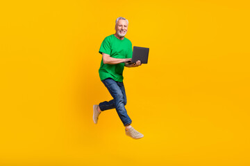 Fototapeta na wymiar Full length photo of handsome aged man jumping run empty space use netbook eshopping isolated on yellow color background
