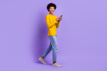 Full size photo of impressed guy dressed yellow long sleeve denim pants hold smartphone staring isolated on purple color background