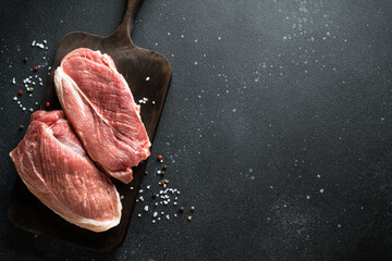 Raw meat steaks with spices, herbs and oil at dark background.