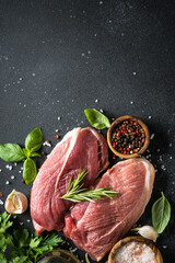 Raw meat steaks with spices, herbs and oil at dark background. Top view with space for text.