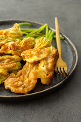 Fried zucchini flowers in batter, a plate with zucchini flowers on a dark background