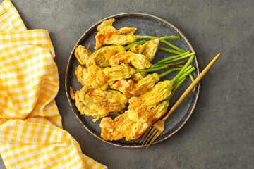 Fried zucchini flowers in batter, a plate with zucchini flowers on a dark background, top view