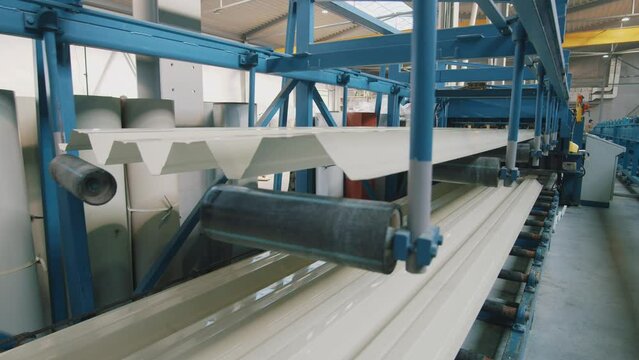 In factory metal sheet forming machine. Steel rollers in metalforming machine for production roof tile in factory. People engineers.