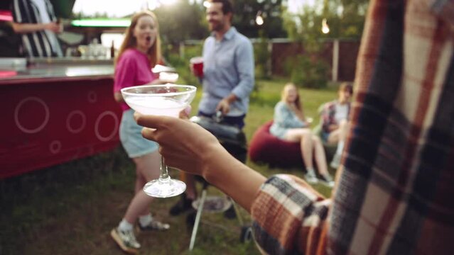 Group of young people, cheerful friends spending good time together at barbecue party outdoors, talking, drinking cocktails. Concept of party, friendship, summer, leisure time, fun and joy