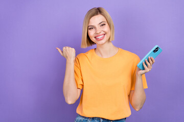 Portrait of optimistic girl dressed stylish clothes indicating at discount empty space hold smartphone isolated on violet color background