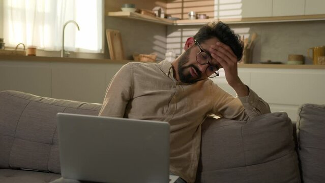 Shocked Upset Indian Arabian Man Guy Business Work From Home Kitchen Negative Bad Result Worried Anxious Male Freelancer On Couch Sofa Read Laptop Notification Computer Problem Fail Difficult Crisis