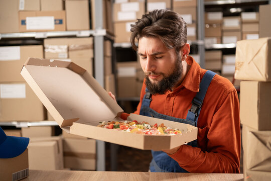 Male staff smiling while holding delicious pizza in warehouse. Lunch in freight transportation and distribution warehouse. Industrial and industrial workers concept