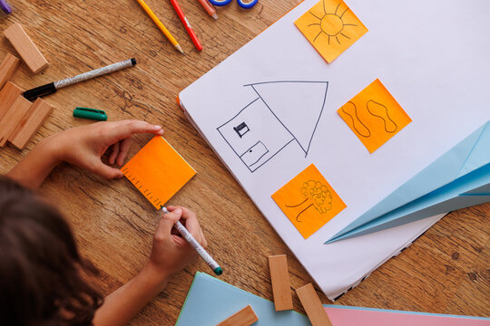 boy draws a house. the child makes a layout of the house. the boy is engaged with scissors and paper. the child is engaged in creativity at home.