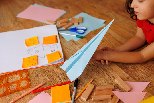 child makes a model of an airplane out of paper. the boy is engaged with scissors and paper. the child is engaged in creativity at home.