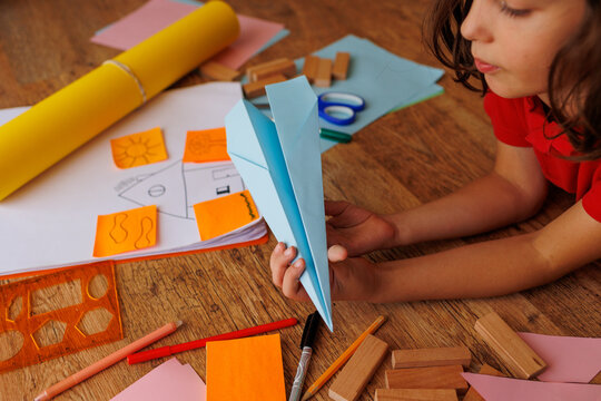 child makes a model of an airplane out of paper. the boy is engaged with scissors and paper. the child is engaged in creativity at home.