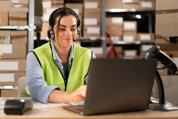 Portrait of a smiling warehouse staff listening and talking to a customer using a headset while...