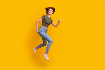 Full length photo of adorable excited girl dressed khaki top jumping high running empty space isolated yellow color background