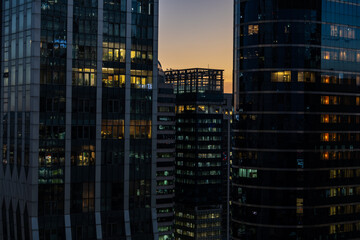 Fototapeta na wymiar Offices seen through illuminated windows after sunset, modern city night view with reflections in architecture