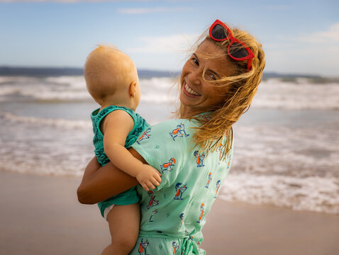 Smiling young mother and baby son spending time on sandy beach. Summer vacation. Happy family relationships. Sunny bright day. Seminyak beach, Bali, Indonesia