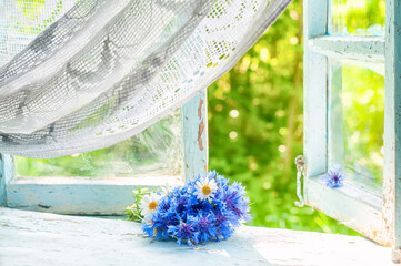 Nice vintage photo. a bouquet of wild flowers of daisies and blue cornflowers on an old open window to the garden.